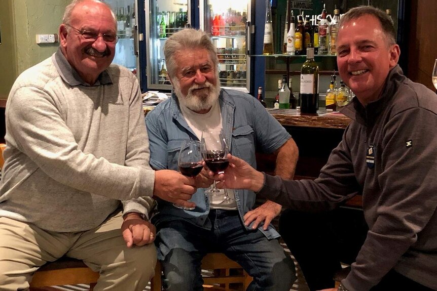 Three men sharing a glass of red wine during the Nullarbor Links golf tournament Chasing The Sunset