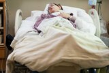 A young woman lies in a hospital bed.