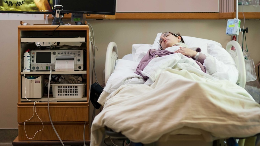 A woman in a hospital bed holds her newborn baby.