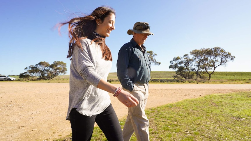 A woman and a man walk across an open field smiling.