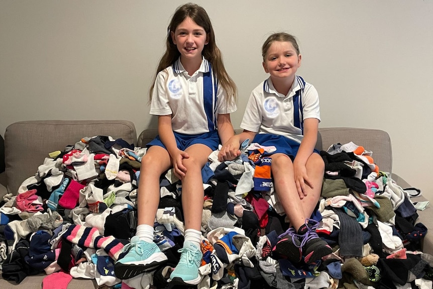 Two dark haired young girls sit on a large pile of socks.