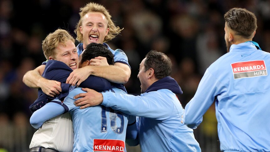 Sydney FC players and staff leap into each others' arms in celebration.