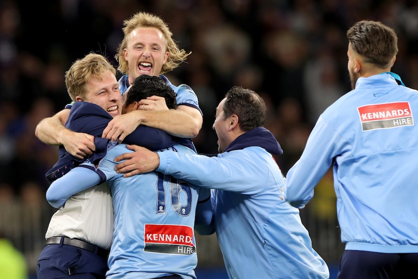 Sydney FC players and staff leap into each others' arms in celebration.