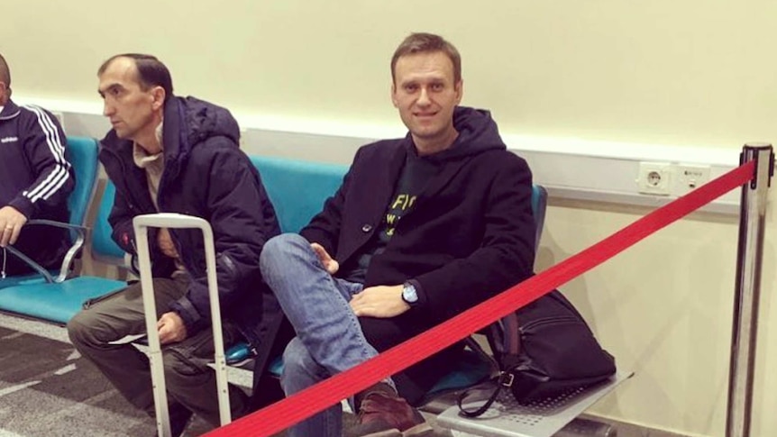 Russian critic Alexei Navalny sits down at an airport and is behind a red rope