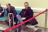 Russian critic Alexei Navalny sits down at an airport and is behind a red rope