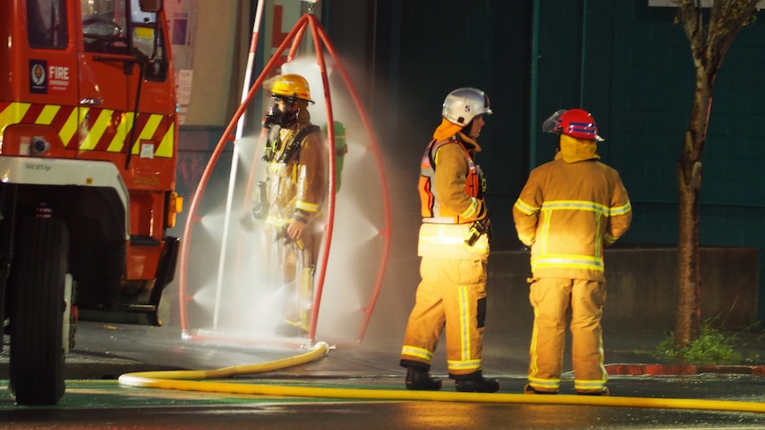 Three firefighters stand outside in the dark in Wellington with one being sprayed with sprinklers