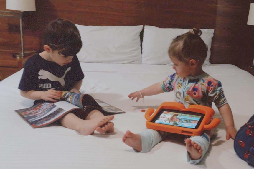 Two children playing on a bed in hotel quarantine