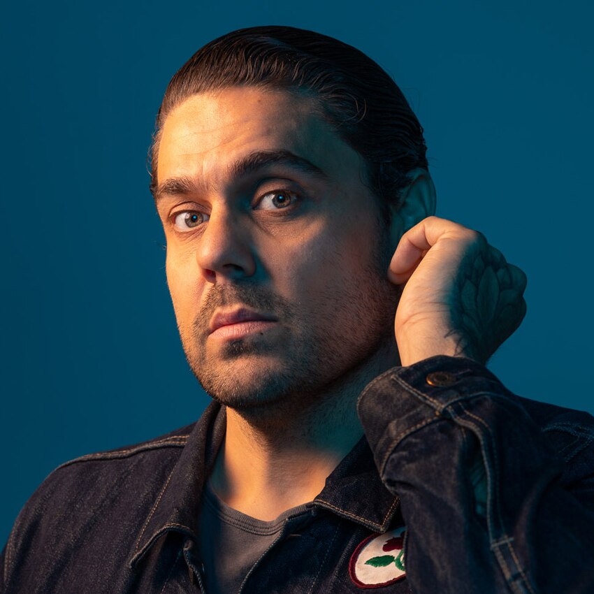 A headshot of Dan Sultan posed before a dark teal background.
