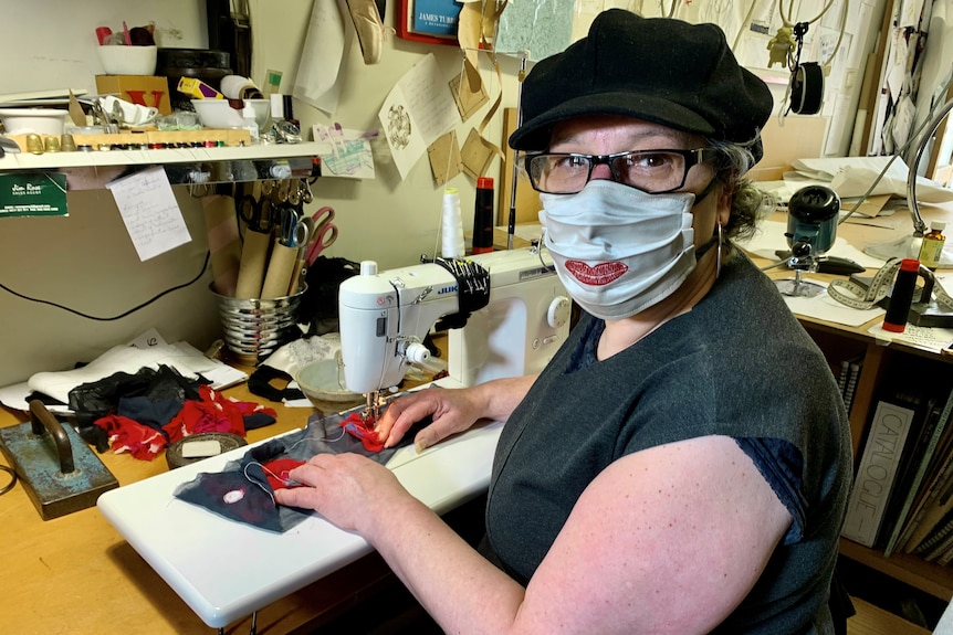 Viv Dourali sits at her sewing machine, while wearing a mask with red lips printed on it