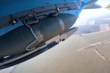 Close-up of a bomb being carried under a fighter jet taking off. 
