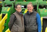 Two women stand in front of a green and yellow machine