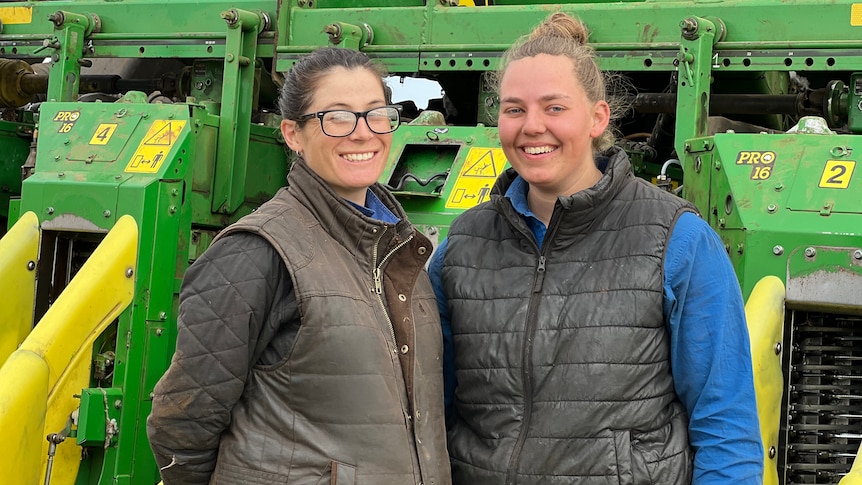 Two women stand in front of a green and yellow machine