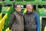 Two women stand in front of a green and yellow machine