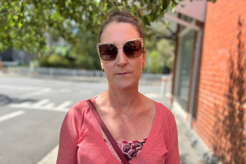 Christine Maynard, woman wearing a pink shirt and sunglasses, looks at the camera.