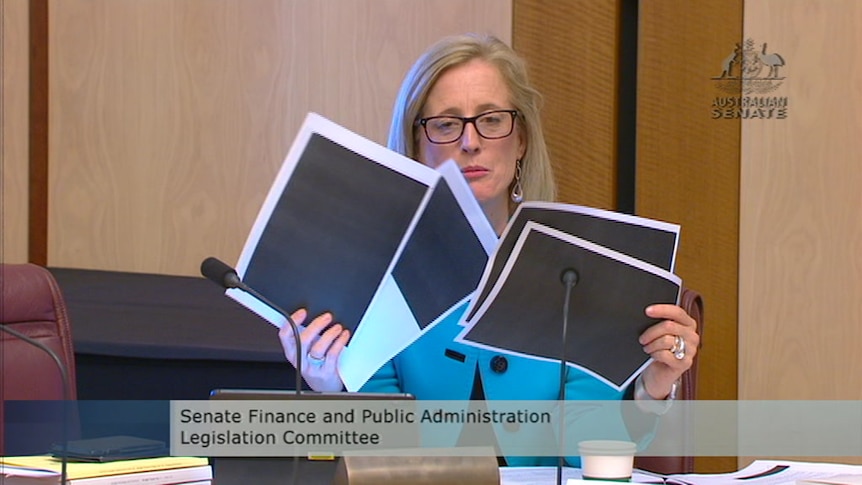 Katy Gallagher holds up pages fully blacked out