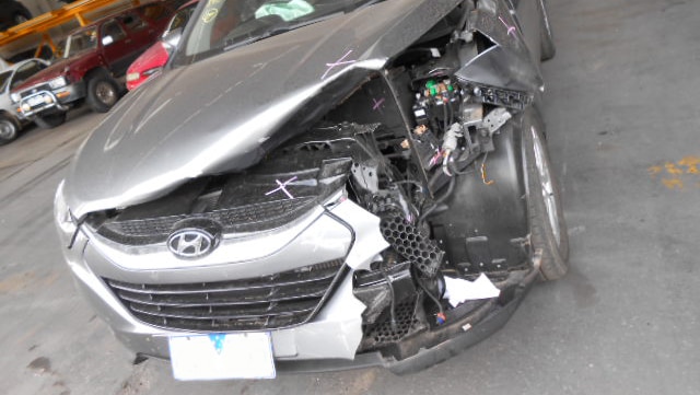 A silver car with substantial damage pushing up the bonnet and exposing the engine.