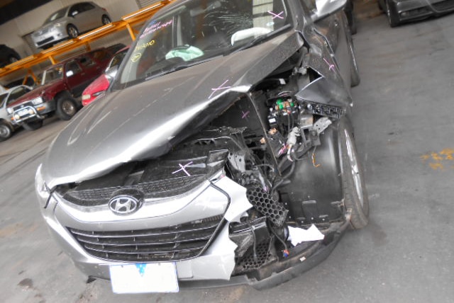 A silver car with substantial damage pushing up the bonnet and exposing the engine.