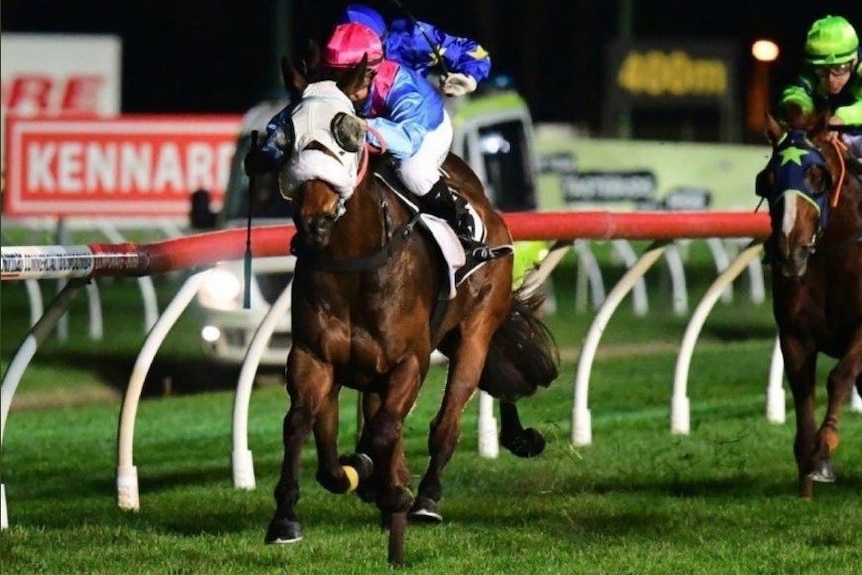 Jockey riding a brown horse on a track at night-time.