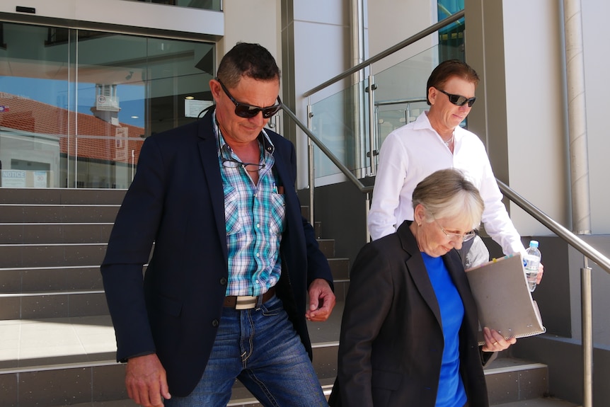 Two men with sunglasses and a woman in a blue shirt walking down steps outdoors