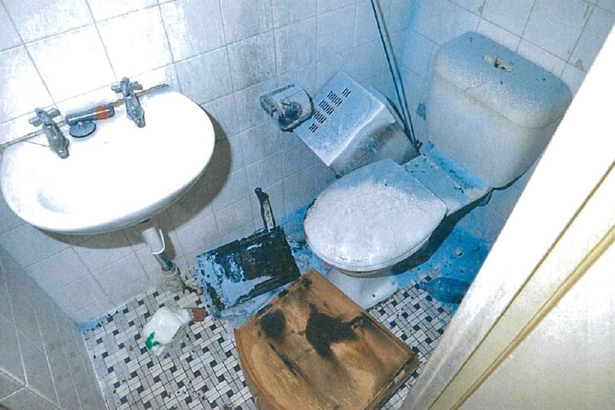 A bathroom with a burnt chest of drawers and microwave on the floor