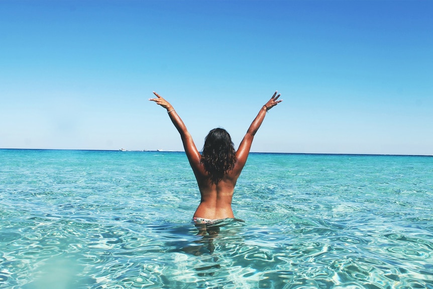 A woman holds her arms up while standing in the ocean.