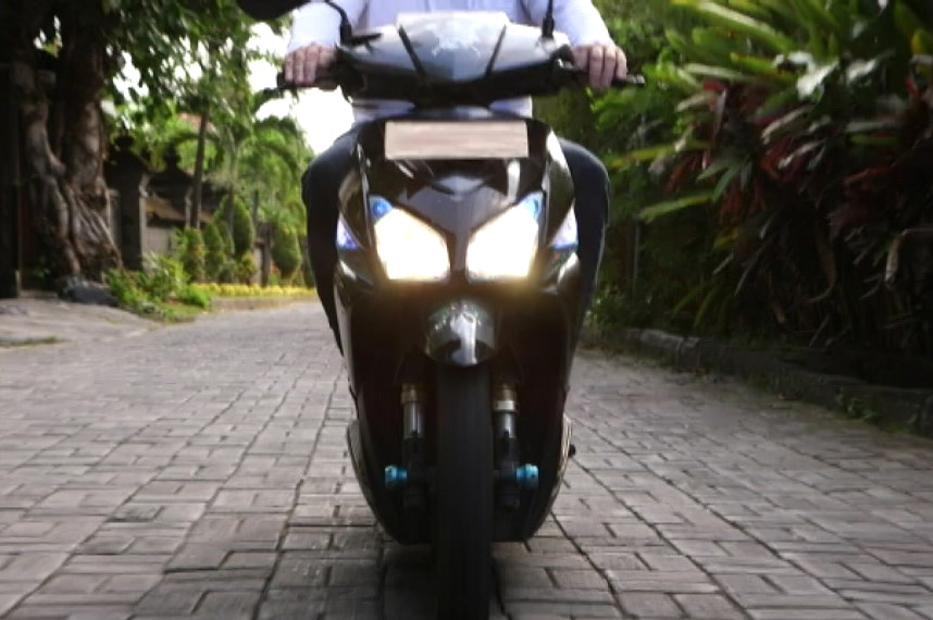 Dog investigator Luke rides down a Bali street on a scooter.