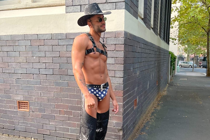 a scantily clad man in a cowboy hat waiting on the street