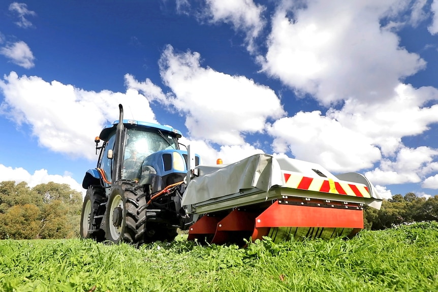 A tractor pushes a box-like contraption over grass.