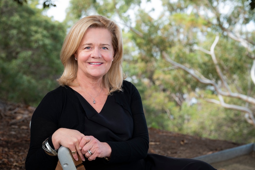 Mid shot of a woman wearing black sitting on a chair in a bushland setting.