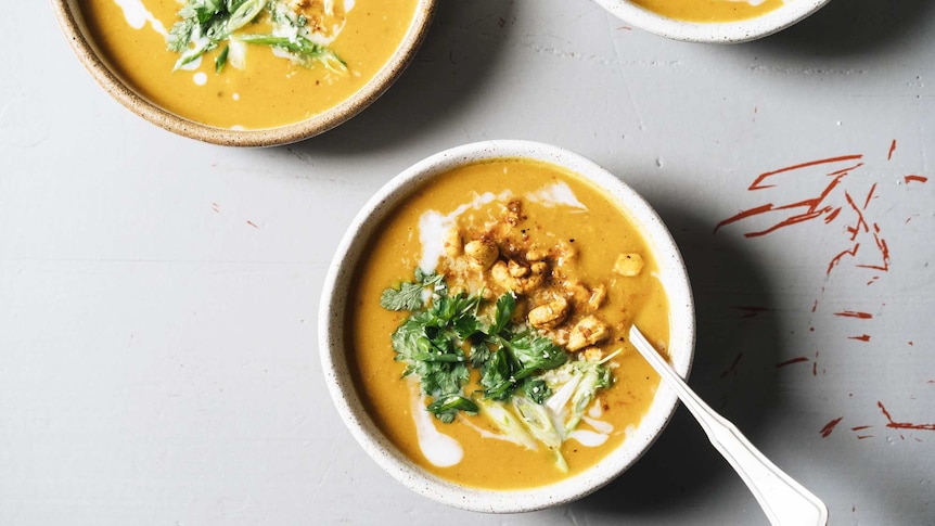 Three bowls of spiced pumpkin soup topped with coconut milk, roasted curry cashews, coriander, for a warming vegetarian dinner.