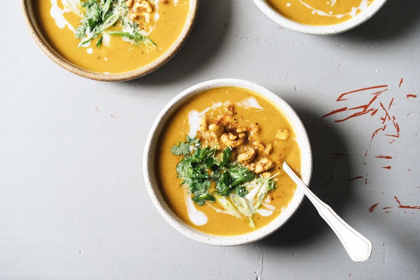 Three bowls of spiced pumpkin soup topped with coconut milk, roasted curry cashews, coriander, for a warming vegetarian dinner.