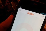 An image of someone holding a phone with the Tinder app open.