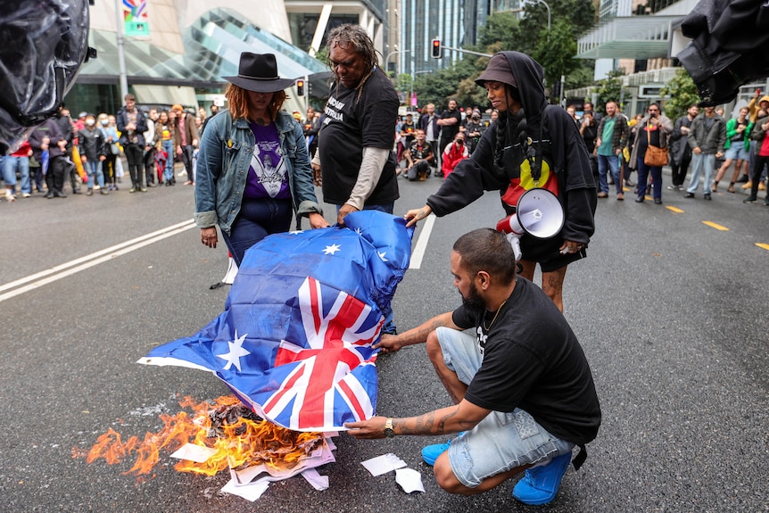 Four activists are seen burning an Australian flag during a rally on a Brisbane street.