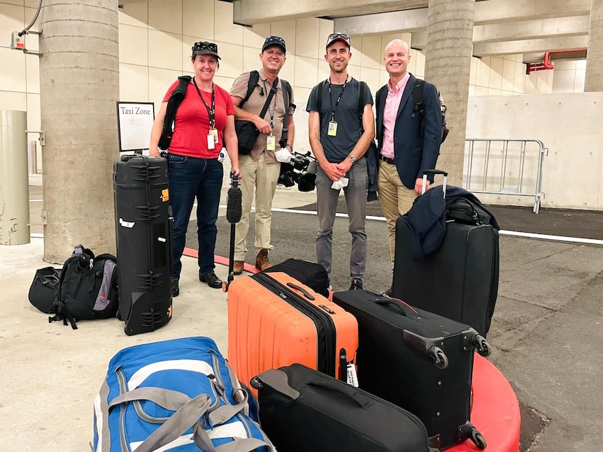 One woman and three men standing with suitcases and camera equipment.