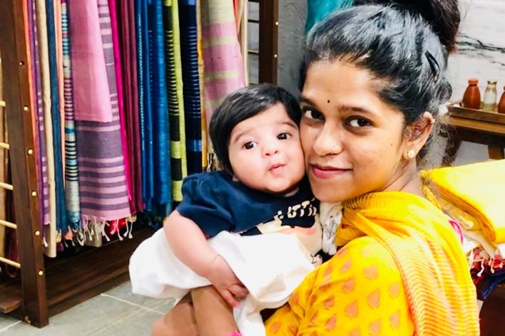 Divya Gagula sitting in a chair holding her baby daughter Shaivi