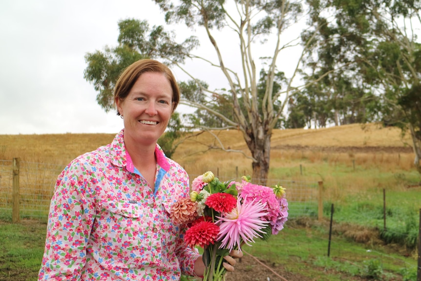 A woman stands in with a bunch of dahlias in front of a paddock