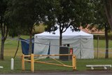 A white tent set up behind police tape in a park.