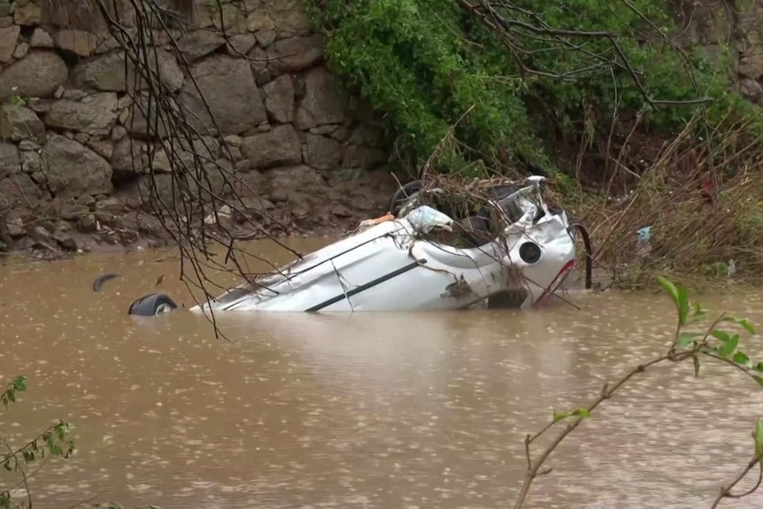A white car upside down and mostly under water.