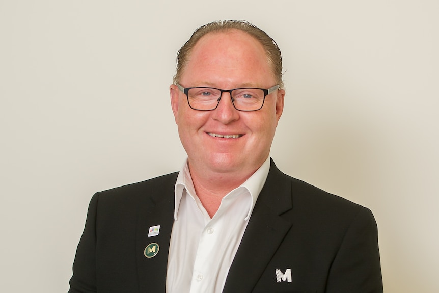 A middle-aged man in a suit looks at the camera