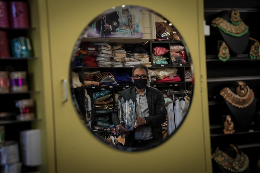 A mirror reflection of Raj Shah, who is holding clothing in his shop 