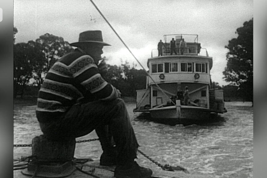 A black and white image of a man sitting as a paddle steamer is towed on water.
