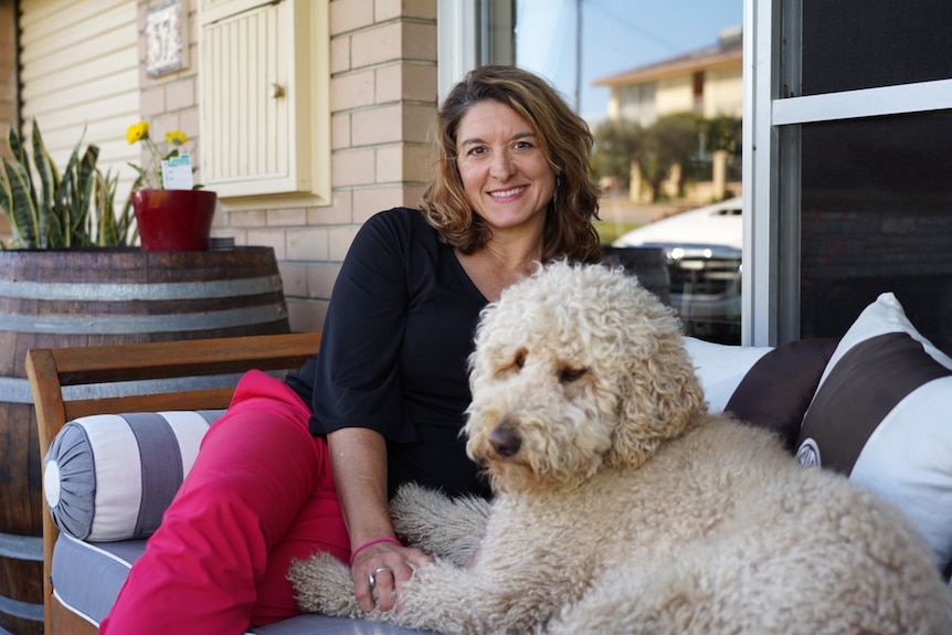 A woman sits on an outdoor sofa with a large dog.