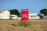 A red auction sign on an empty block of land