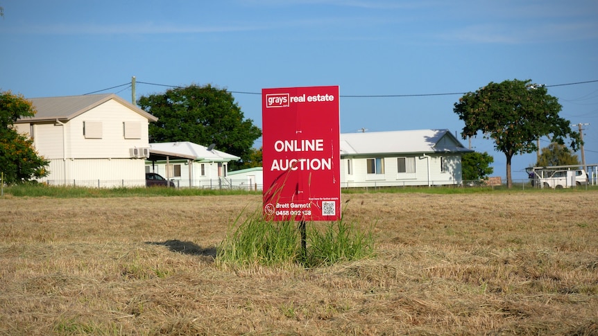 A red auction sign on an empty block of land