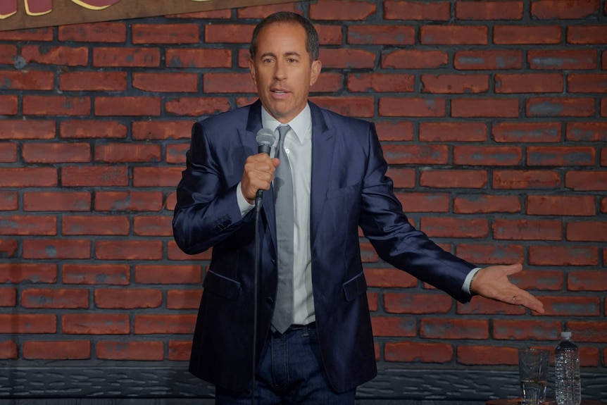 Comedian Jerry Seinfeld stands on stage during a stand-up show.