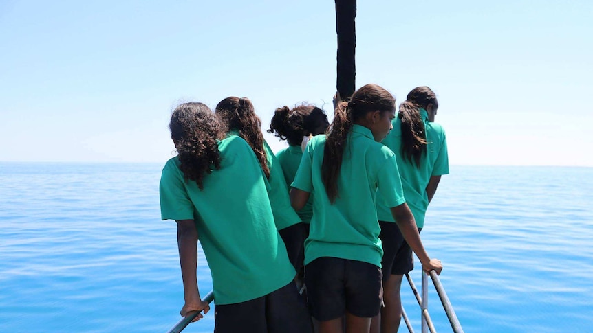 Girls from  the Broome Senior High School are standing on the bow of a sailing boat, looking for whales.