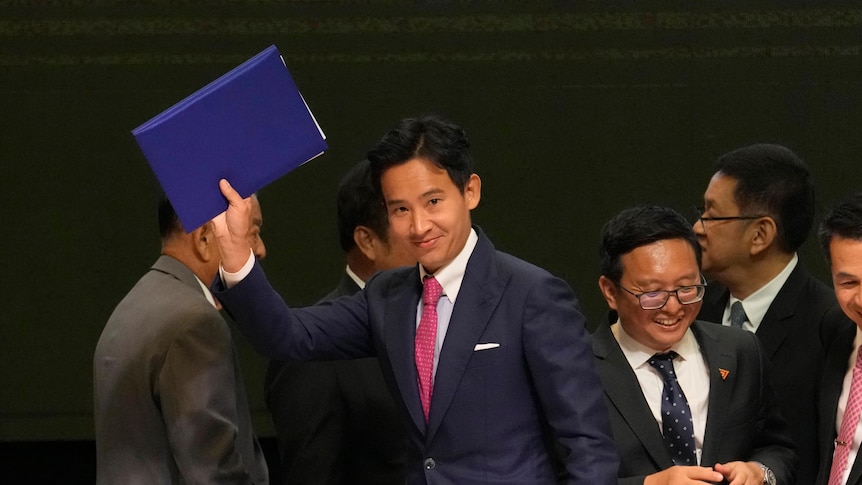 A young Thai man in suit with red tie gestures with a blue folder.