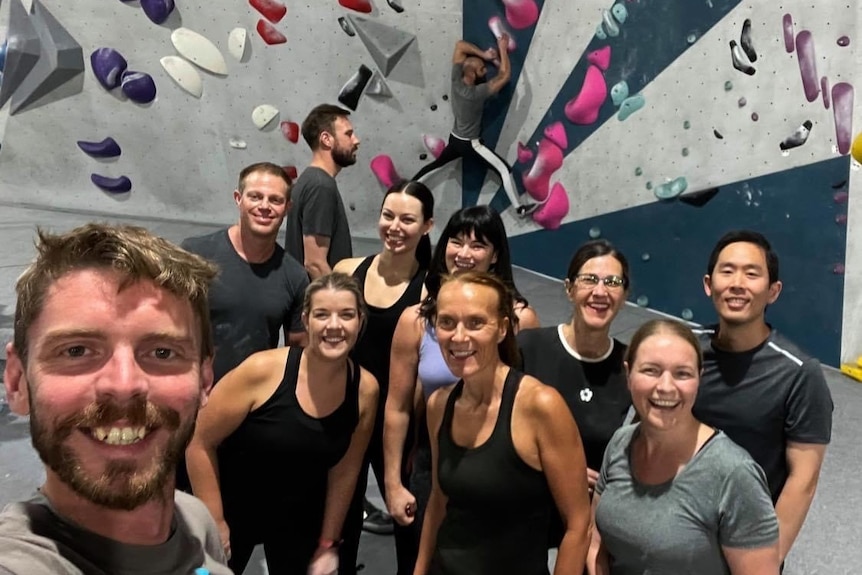 A group of people in sports clothing pose inside a rock climbing gym 