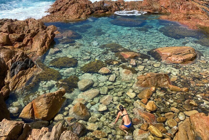 A girl begins swimming in a beautiful rockpool