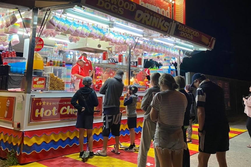 People line up outside roadside stall selling dagwood dogs at night.